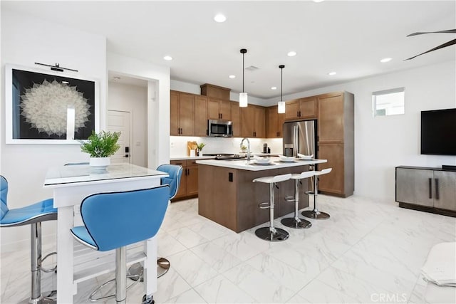 kitchen with a breakfast bar, decorative light fixtures, stainless steel appliances, and an island with sink