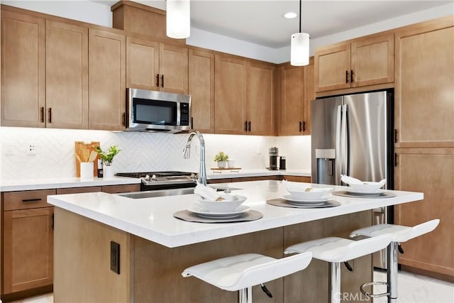 kitchen featuring a kitchen bar, appliances with stainless steel finishes, backsplash, a center island with sink, and decorative light fixtures