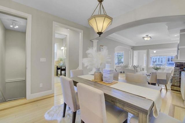 dining area with a fireplace, a tray ceiling, and light wood-type flooring