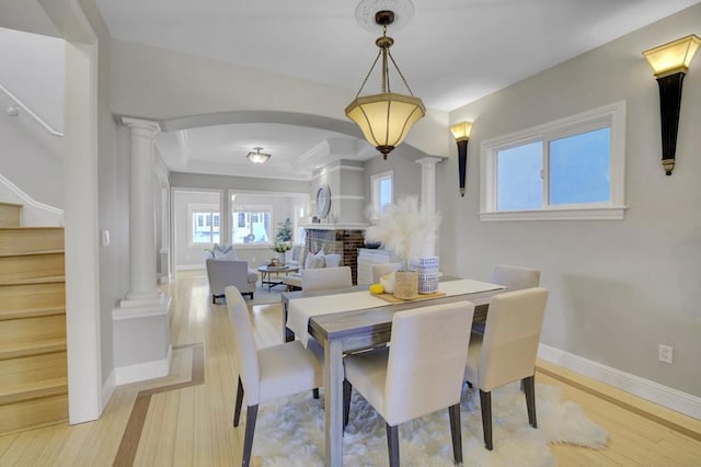 dining space featuring light wood-type flooring, a fireplace, and ornate columns