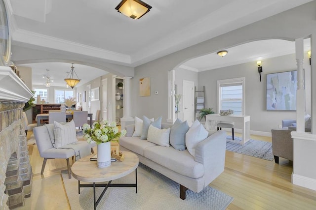 living room with a brick fireplace, light hardwood / wood-style flooring, crown molding, and ornate columns