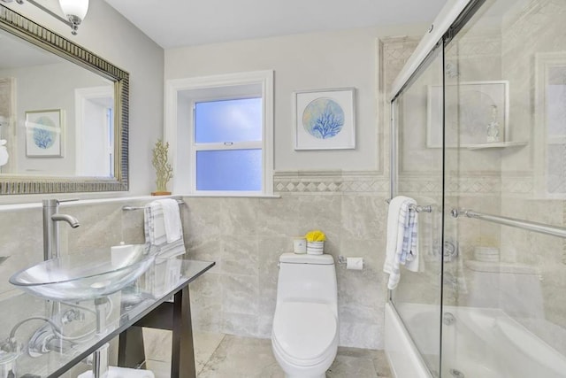 full bathroom featuring bath / shower combo with glass door, tile walls, toilet, and sink