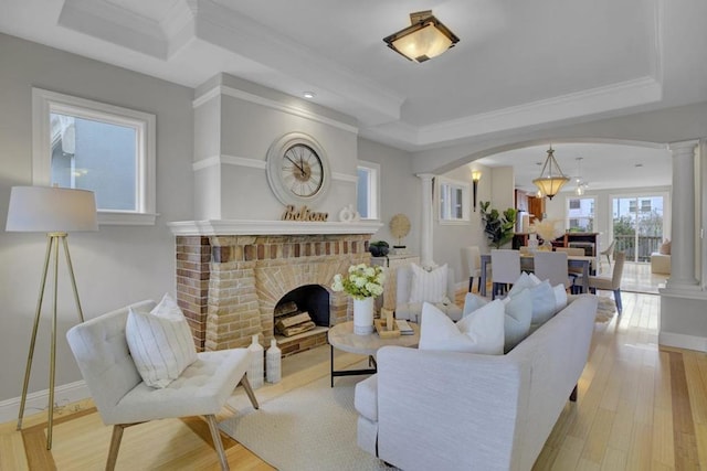 living room featuring light hardwood / wood-style floors, crown molding, decorative columns, and a brick fireplace