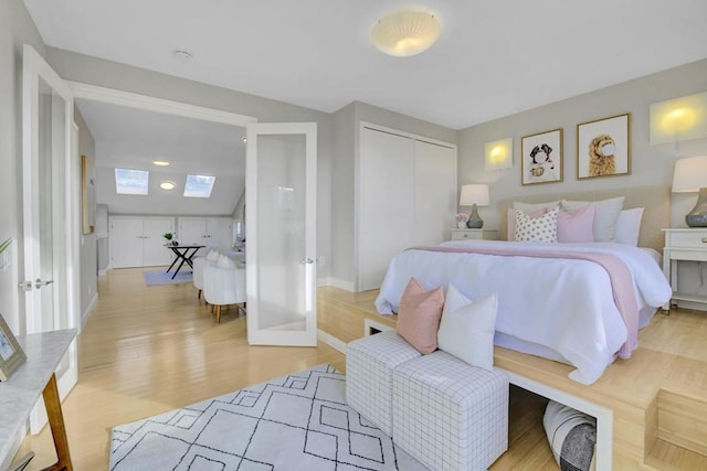 bedroom featuring a closet, light hardwood / wood-style floors, french doors, and lofted ceiling with skylight