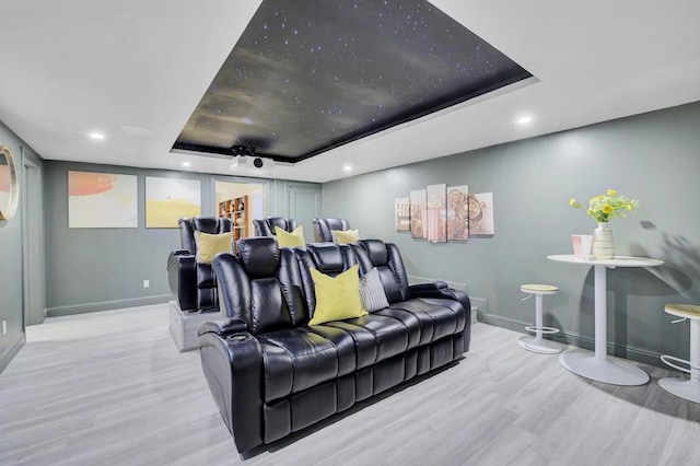 cinema with light hardwood / wood-style floors and a raised ceiling