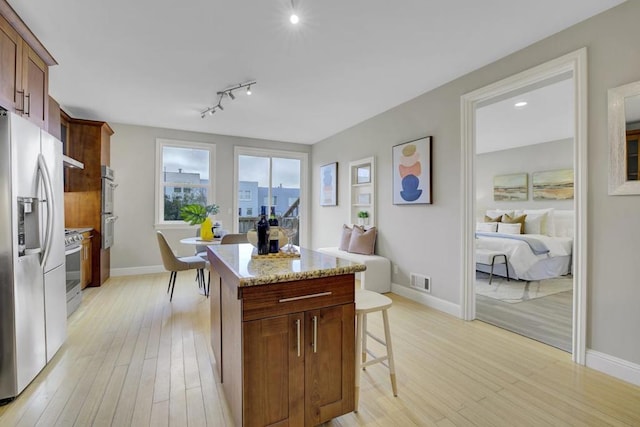 kitchen featuring light stone counters, appliances with stainless steel finishes, light hardwood / wood-style flooring, and a center island