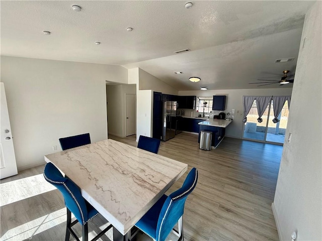 dining room featuring a textured ceiling, light wood-type flooring, vaulted ceiling, and ceiling fan