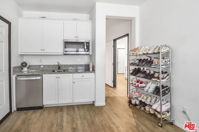 kitchen with appliances with stainless steel finishes, dark stone counters, sink, hardwood / wood-style flooring, and white cabinetry