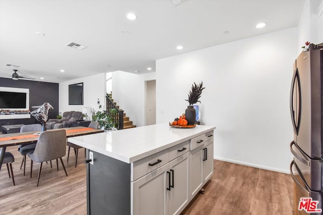 kitchen with ceiling fan, white cabinets, a center island, light hardwood / wood-style floors, and stainless steel refrigerator