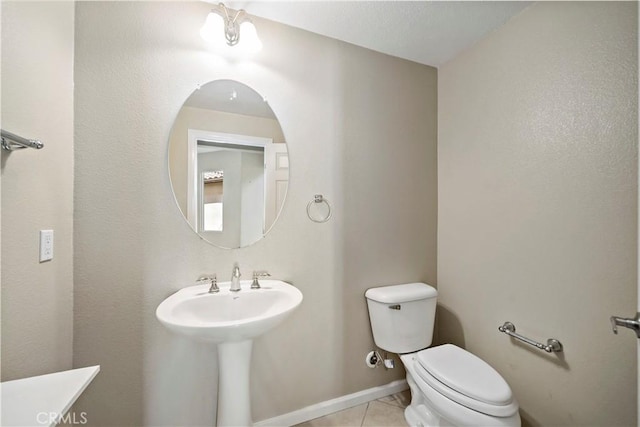 half bathroom with a sink, tile patterned flooring, toilet, and baseboards