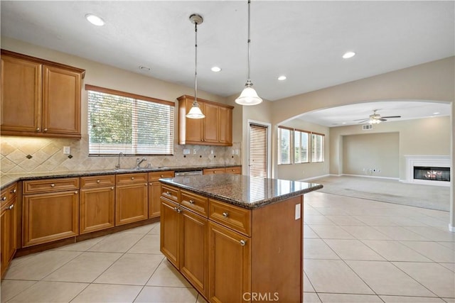 kitchen featuring arched walkways, brown cabinets, decorative light fixtures, and a center island