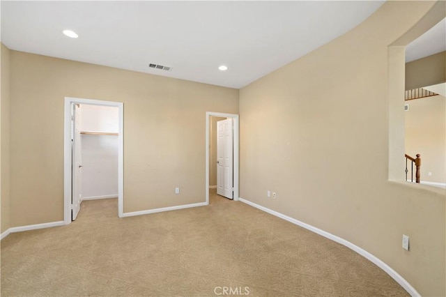 unfurnished bedroom featuring light colored carpet, a walk in closet, visible vents, and baseboards