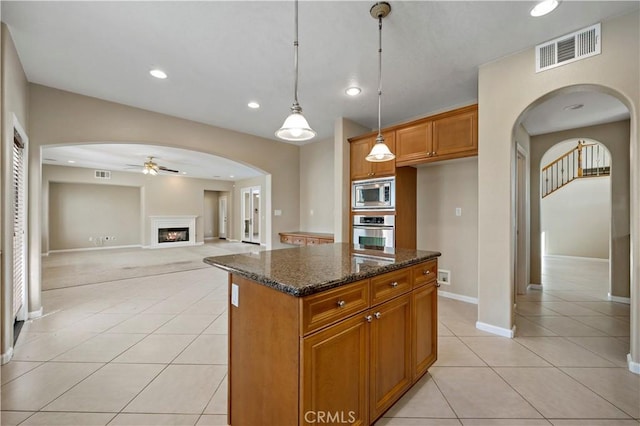 kitchen with a center island, brown cabinets, visible vents, appliances with stainless steel finishes, and dark stone counters