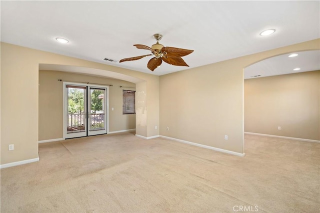 spare room with a ceiling fan, arched walkways, light carpet, and baseboards