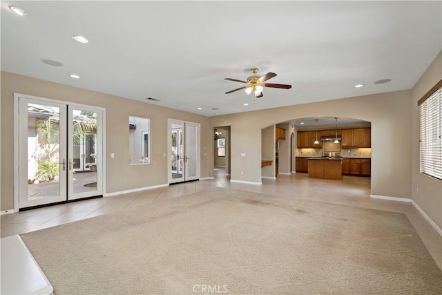 unfurnished living room featuring arched walkways, light tile patterned floors, recessed lighting, light carpet, and baseboards