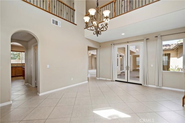 unfurnished room featuring light tile patterned floors, arched walkways, a high ceiling, visible vents, and baseboards