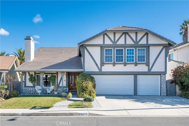 tudor house featuring a front yard, covered porch, and a garage