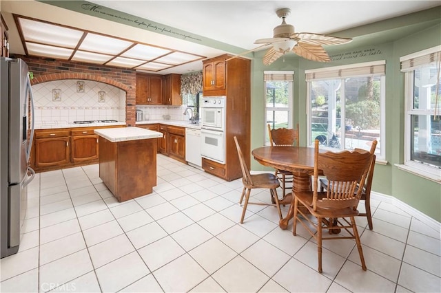 kitchen featuring white appliances, a kitchen island, tasteful backsplash, ceiling fan, and light tile patterned floors