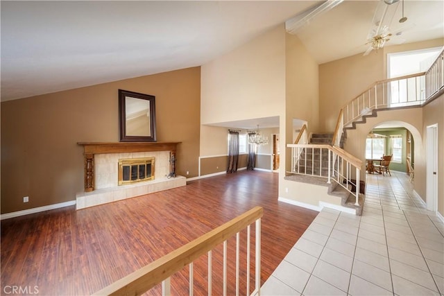 unfurnished living room with ceiling fan with notable chandelier, a fireplace, hardwood / wood-style floors, and high vaulted ceiling