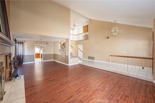 unfurnished living room featuring ceiling fan with notable chandelier, wood-type flooring, a tile fireplace, and high vaulted ceiling