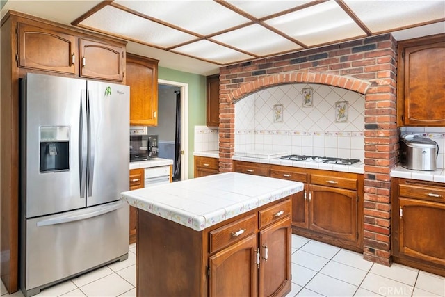 kitchen with a center island, white gas stovetop, stainless steel refrigerator with ice dispenser, tasteful backsplash, and light tile patterned floors