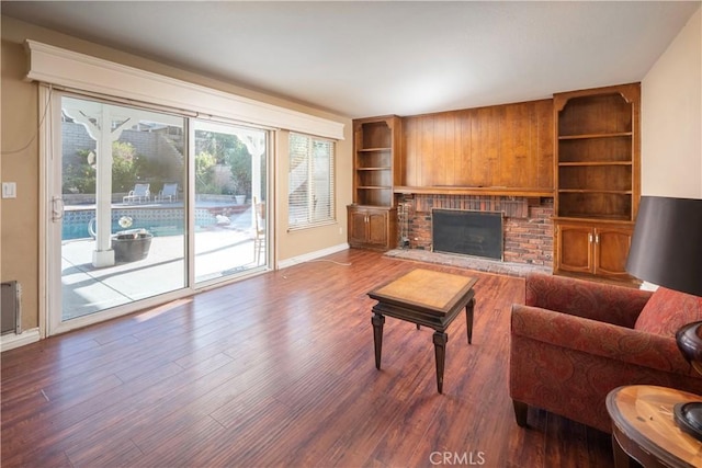 living room featuring a brick fireplace, wood-type flooring, and built in features