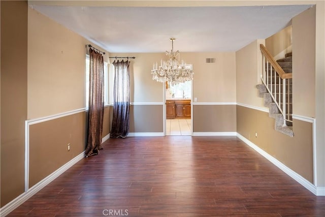 empty room with dark wood-type flooring and an inviting chandelier