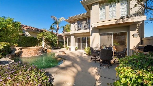 back of property with a patio area, a balcony, and a pool with hot tub