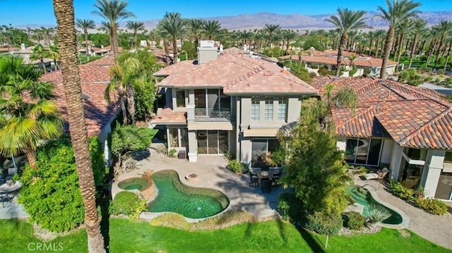 rear view of property with an in ground hot tub, a balcony, a patio, and a mountain view