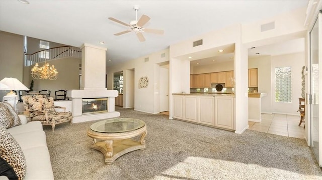 living room featuring a wealth of natural light, a large fireplace, light colored carpet, and ceiling fan with notable chandelier