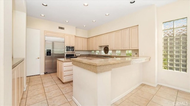 kitchen featuring cream cabinetry, light tile patterned floors, kitchen peninsula, and appliances with stainless steel finishes