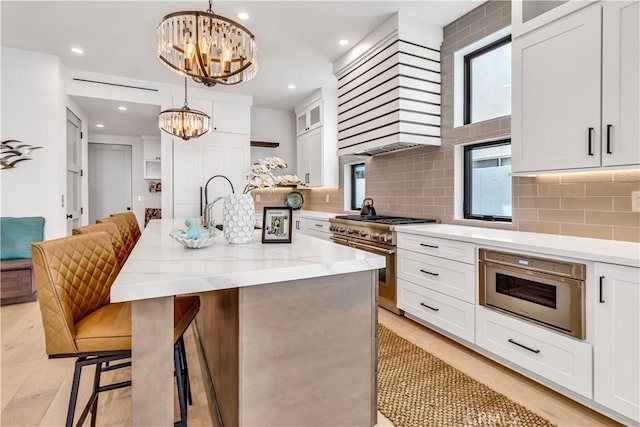 kitchen featuring white cabinets, an inviting chandelier, hanging light fixtures, high end stove, and a center island with sink