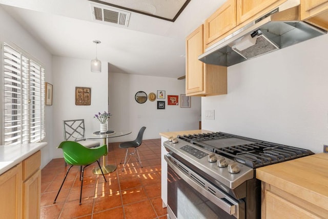 kitchen with stainless steel gas stove, dark tile patterned floors, light brown cabinetry, and decorative light fixtures