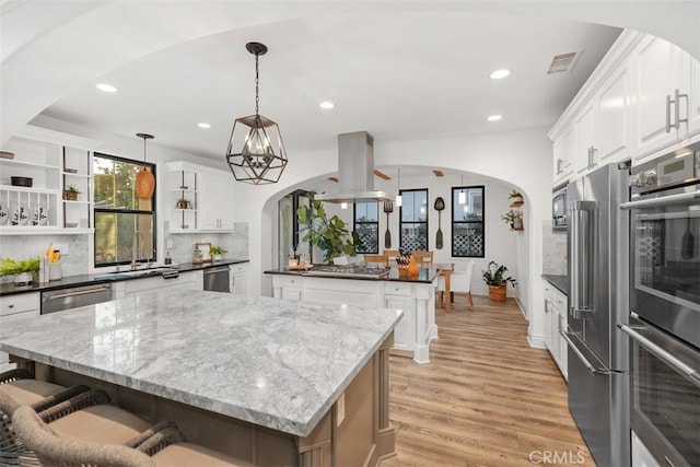 kitchen with white cabinetry, a center island, hanging light fixtures, decorative backsplash, and island range hood