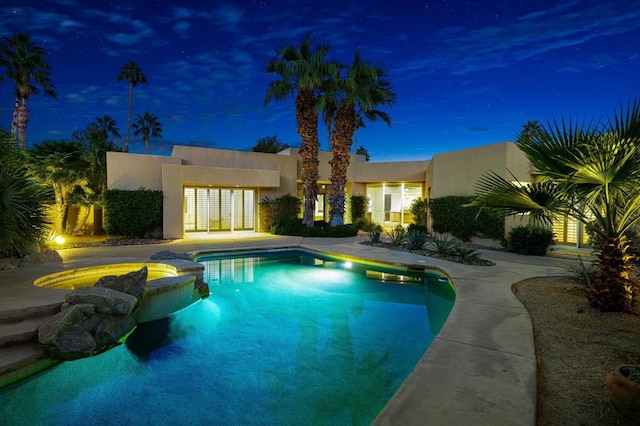 pool at night featuring an in ground hot tub and french doors