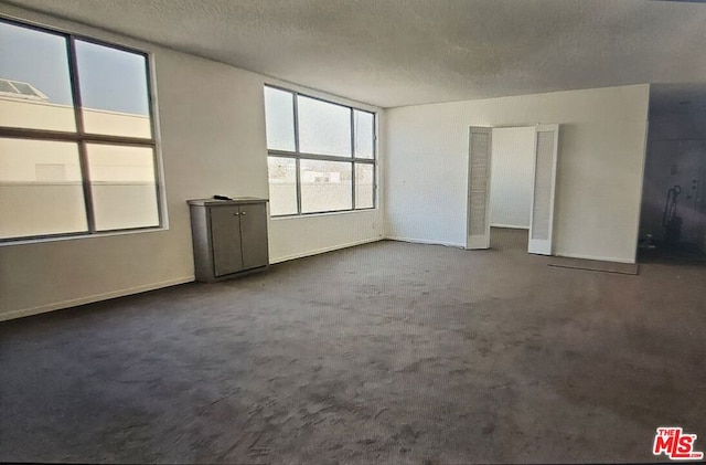 unfurnished room with a textured ceiling and dark colored carpet