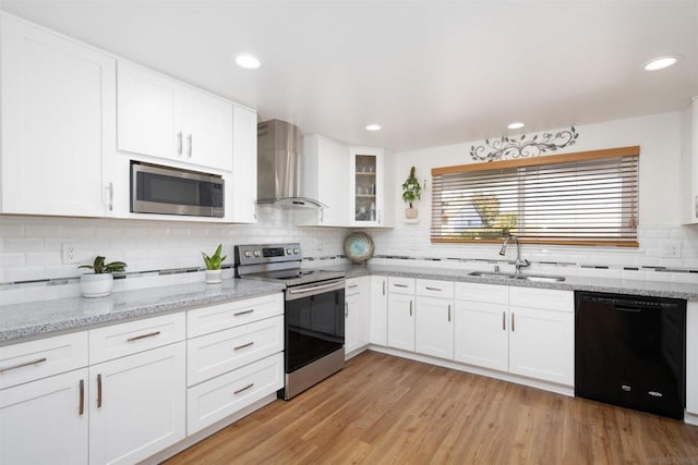 kitchen with white cabinetry, sink, stainless steel appliances, wall chimney range hood, and light hardwood / wood-style flooring