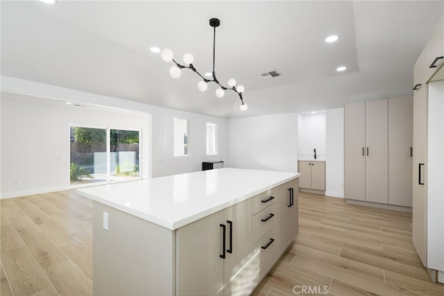 kitchen with white cabinetry, a notable chandelier, pendant lighting, a kitchen island, and light wood-type flooring