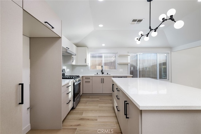 kitchen with pendant lighting, stainless steel range with gas cooktop, light hardwood / wood-style flooring, vaulted ceiling, and decorative backsplash