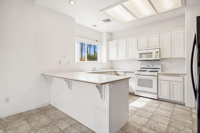 kitchen featuring kitchen peninsula, white appliances, sink, white cabinets, and a breakfast bar area