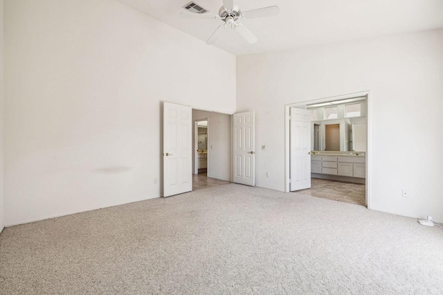 unfurnished bedroom featuring light carpet, a towering ceiling, ceiling fan, and connected bathroom