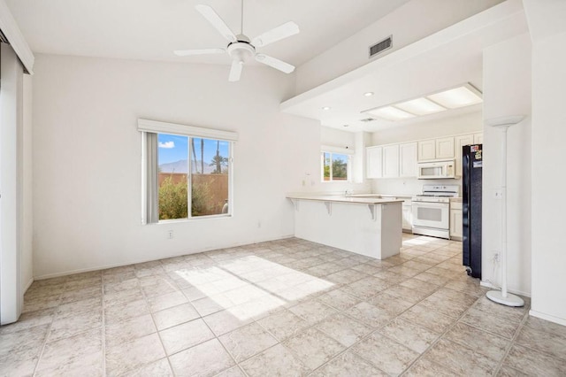 kitchen with white appliances, a kitchen breakfast bar, kitchen peninsula, plenty of natural light, and white cabinetry