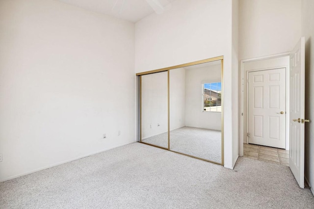 unfurnished bedroom featuring a closet, a towering ceiling, and light colored carpet