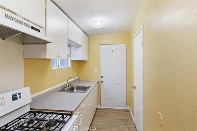 kitchen with white cabinets, white gas range, light countertops, under cabinet range hood, and a sink