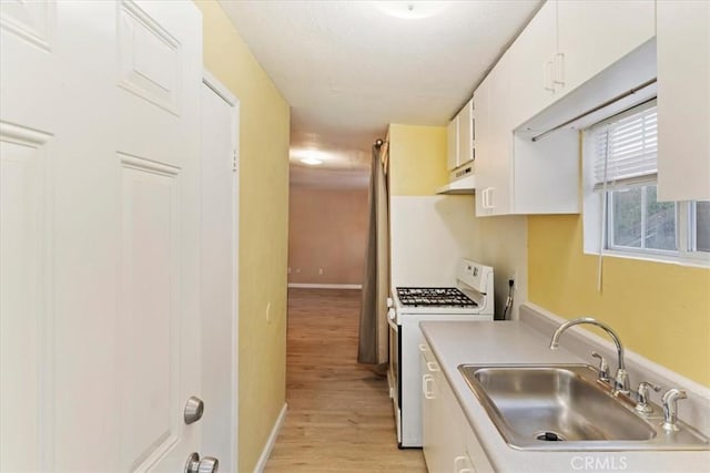 kitchen featuring white gas range, light countertops, white cabinetry, a sink, and under cabinet range hood