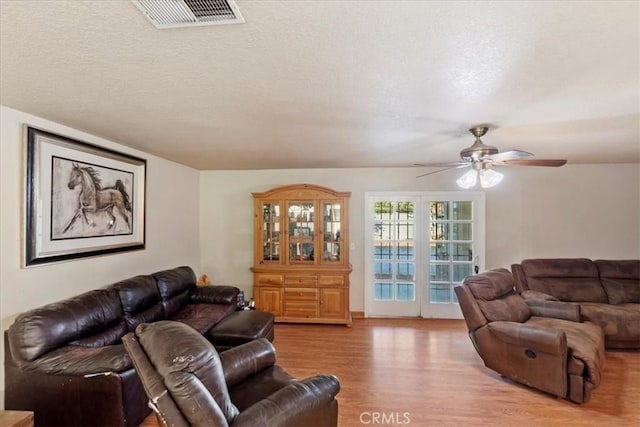 living area featuring a ceiling fan, light wood-type flooring, visible vents, and a textured ceiling