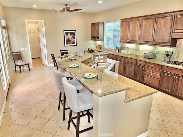 kitchen featuring light stone countertops, an island with sink, sink, a breakfast bar, and light tile patterned floors