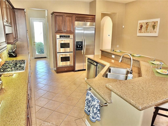 kitchen with stainless steel appliances, sink, a kitchen breakfast bar, light tile patterned flooring, and light stone counters