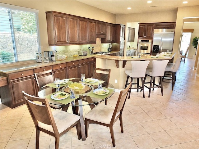 kitchen with a kitchen breakfast bar, backsplash, light tile patterned floors, a center island, and stainless steel appliances