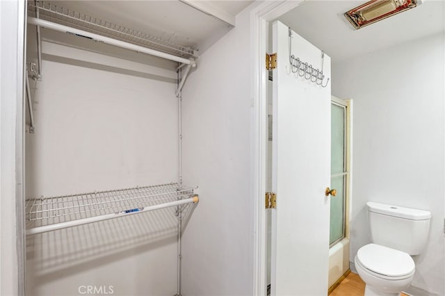 bathroom featuring toilet and combined bath / shower with glass door